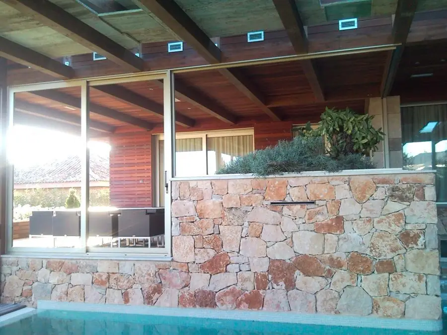 Piscina cubierta con ventanales de aluminio y muro de piedra